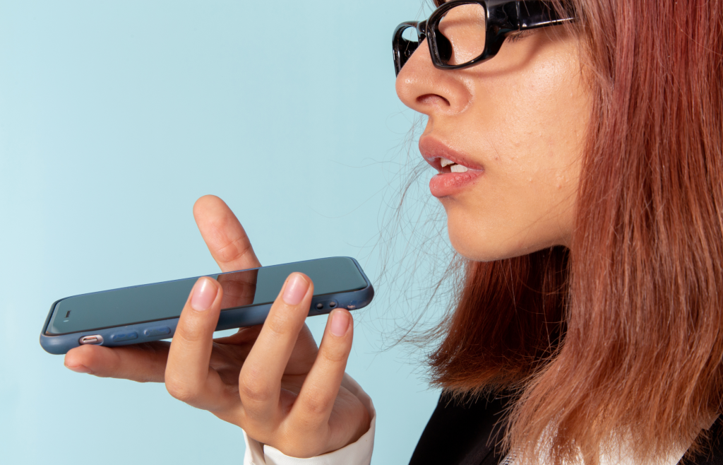 From Keywords to Conversations: How to Optimize Your Guesthouse for AI Assistants 1 A woman using voice search on her mobile phone to find travel accommodations, illustrating the shift toward conversational AI and AEO for guesthouses.