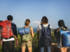 Adventure Tourism-How Hospitality Can Win Travellers with Scuffed Boots and Green Hearts Four young adventure travellers with large backpacks and hiking gear standing on a ridge overlooking a vast green valley under a clear blue sky.